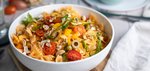 Mediterraner Nudelsalat mit Farfalle, Oliven, Tomaten, Rucola in einer weißen Salatschüssel auf einem Tisch