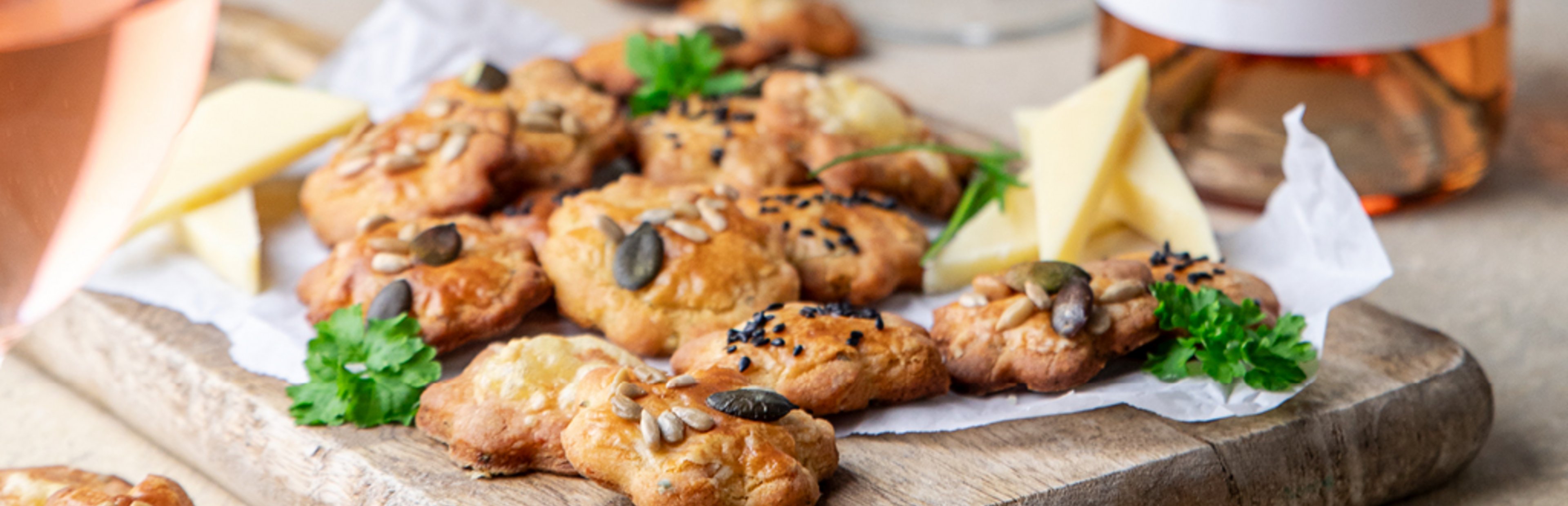 Käsegebäck auf einem Küchenholzbrett. Im Hintergrund eine Falsche Cuvée rose von bioladen*