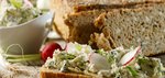 Eine Scheibe Brot auf einem Holzbrett mit selbstgemachten Kräuterfrischkäse und Radieschen belegt. Im Hintergrund ein paar weitere Scheiben Brot und eine weiße Schale mit dem Kräuterdip