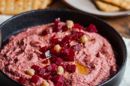 Rote Bete Hummus, angerichtet auf einem tiefen schwarzen Teller, garniert mit kleinen Rote Bete Stückchen.
