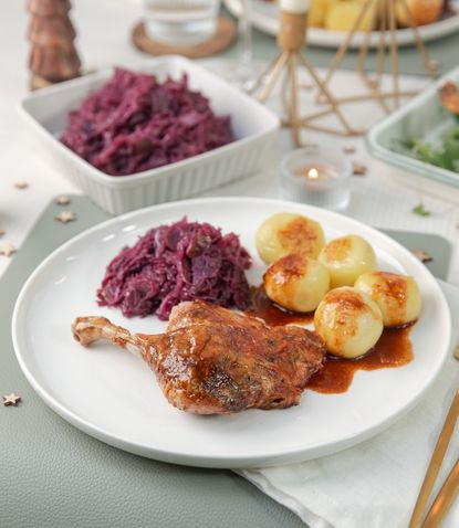 Ein weißer Teller mit Entenkeule, Rotkohl und Kartoffelklößen mit brauner Sauce