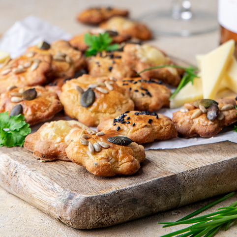 Käsegebäck auf einem Küchenholzbrett. Im Hintergrund eine Falsche Cuvée rose von bioladen*