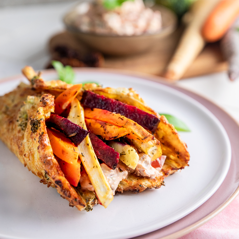 Ein Wrap aus Hüttenkäse gefüllt mit Ofengemüse, angerichtet auf einem weißen Teller.